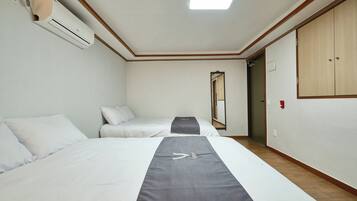 A hotel room with two beds, a ceiling fan, a wall-mounted air conditioner, a mirror, and a wardrobe.
