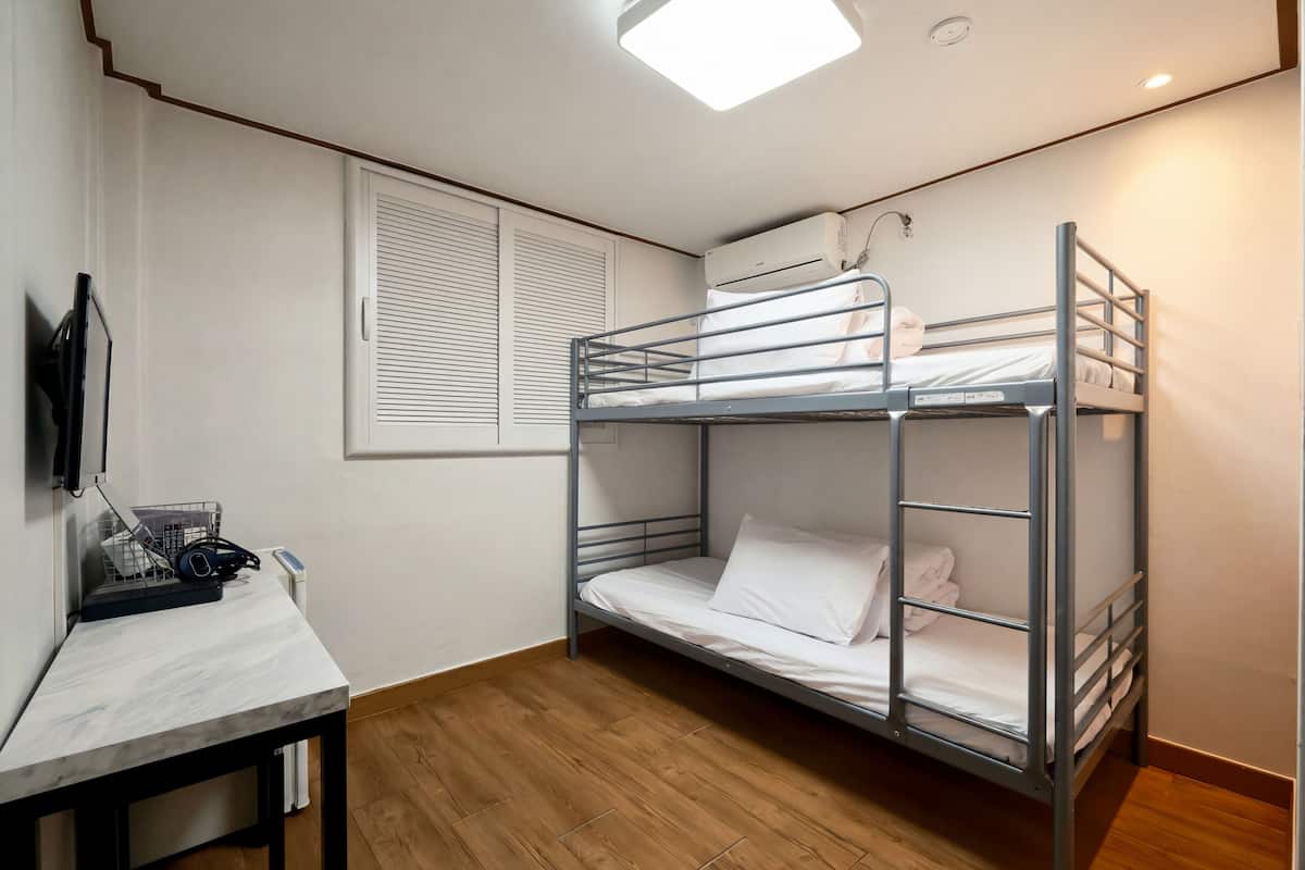 A bunk bed room with a desk, a window with blinds, and an air conditioning unit.