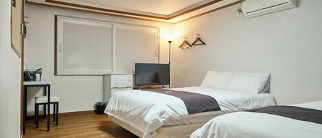 A hotel room with two beds, a desk, a TV, and an air conditioning unit.