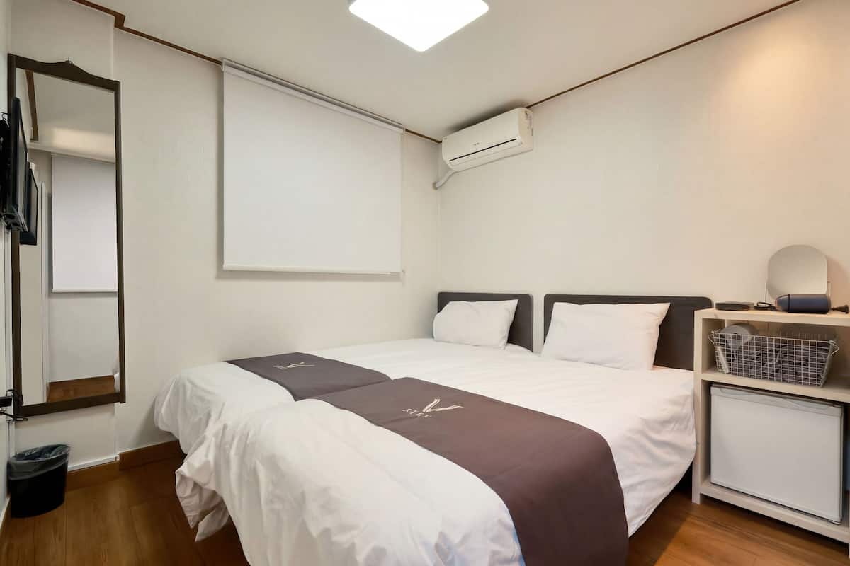 A hotel room with a bed, a nightstand, a mirror, a wall-mounted air conditioner, and a small cabinet.