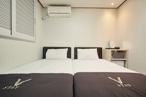 Una cama doble con dos almohadas, una mesita de noche con espejo, y un estante pequeño con una cesta.