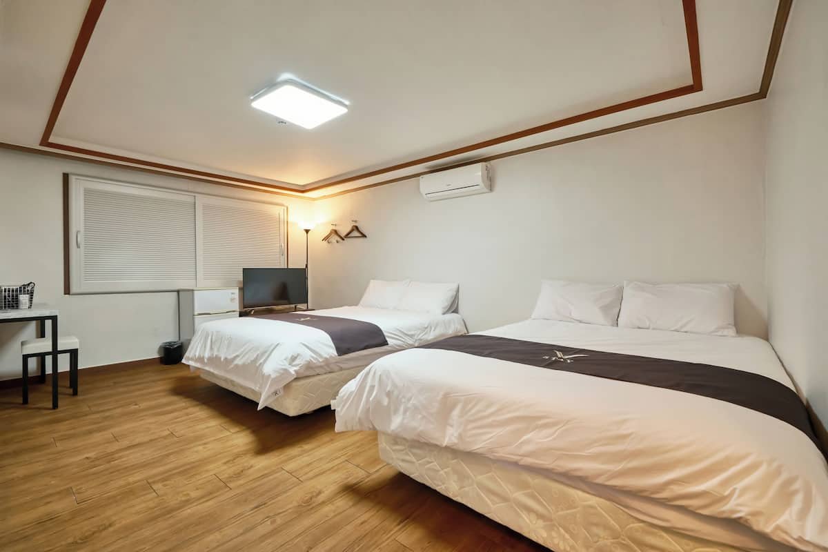 A hotel room with two beds, a desk, a chair, a lamp, and an air conditioning unit.
