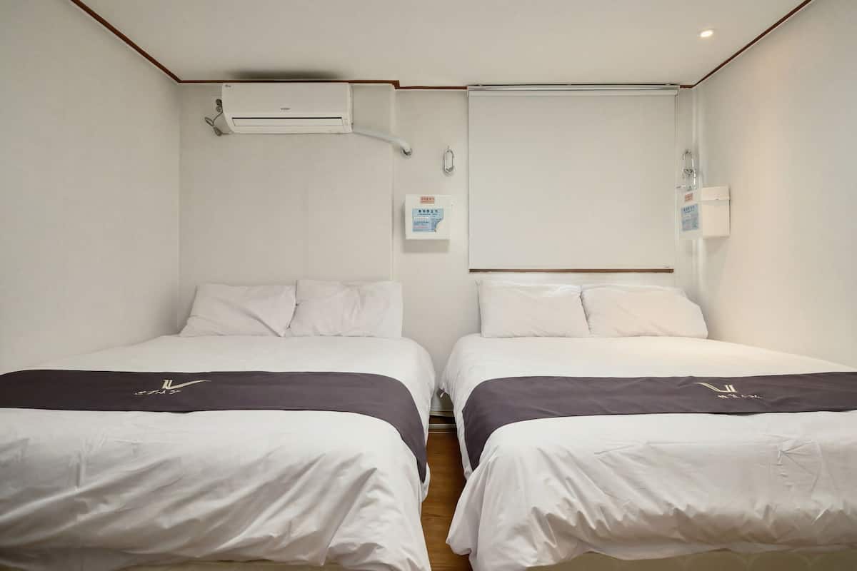 A hotel room with two beds, a wall-mounted air conditioner, a whiteboard, and a small electrical outlet.