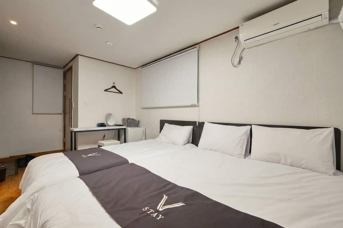 A hotel room with a large bed, a bedside table, a mirror, a hanging light, and a wall-mounted air conditioner.