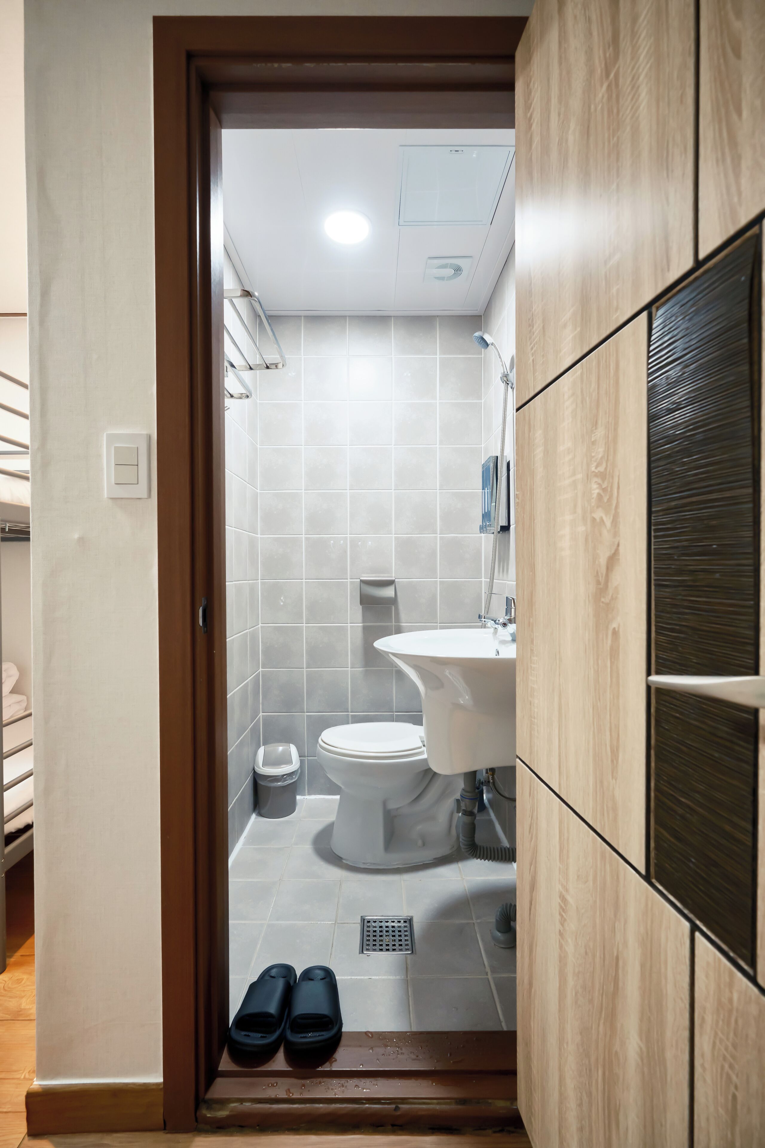 Un baño con inodoro, lavabo y ducha. Hay pantuflas en el suelo.