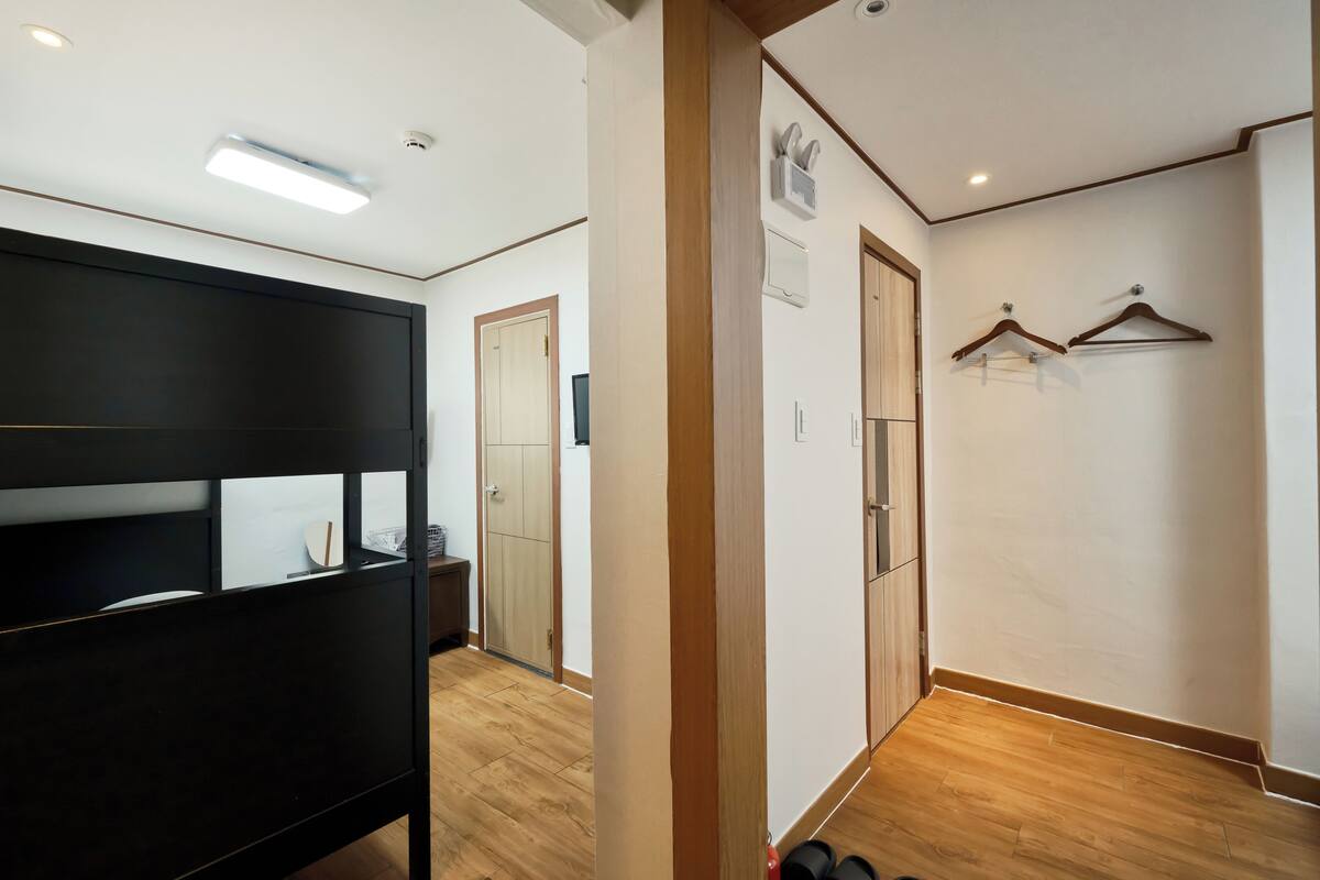 A hallway with a wooden floor, a black partition, and a door leading to a room with a wardrobe and a coat rack.