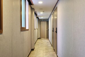 Un pasillo largo y estrecho con suelo de baldosas, puertas a ambos lados y luces empotradas en el techo.