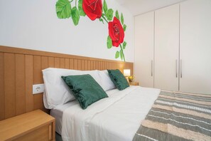 A bedroom with a wooden headboard, white bedding, green pillows, a striped rug, and a wall mural of red roses. - Marina Legacy I Demi-suite Selene 6 (Faro)