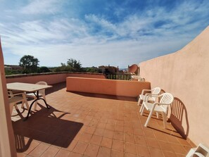 Eine Terrasse im Freien mit Tisch und Stühlen, Blick auf die Landschaft und ein Gebäude im Hintergrund.