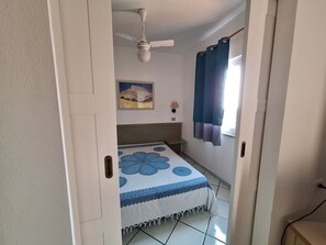 Ein Zimmer mit einem Bett, einem Deckenventilator, einem Gemälde, einer Lampe und einem Fenster mit Vorhängen.