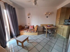 A compact room with a bed, a small table, a chair, a kitchenette, and a ceiling fan. - Cozy three-bedroom ground-floor apartment (Sardegna)