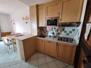 A compact kitchen with wooden cabinets, a microwave, a gas stove, and a sink. - Cozy three-bedroom ground-floor apartment (Sardegna)