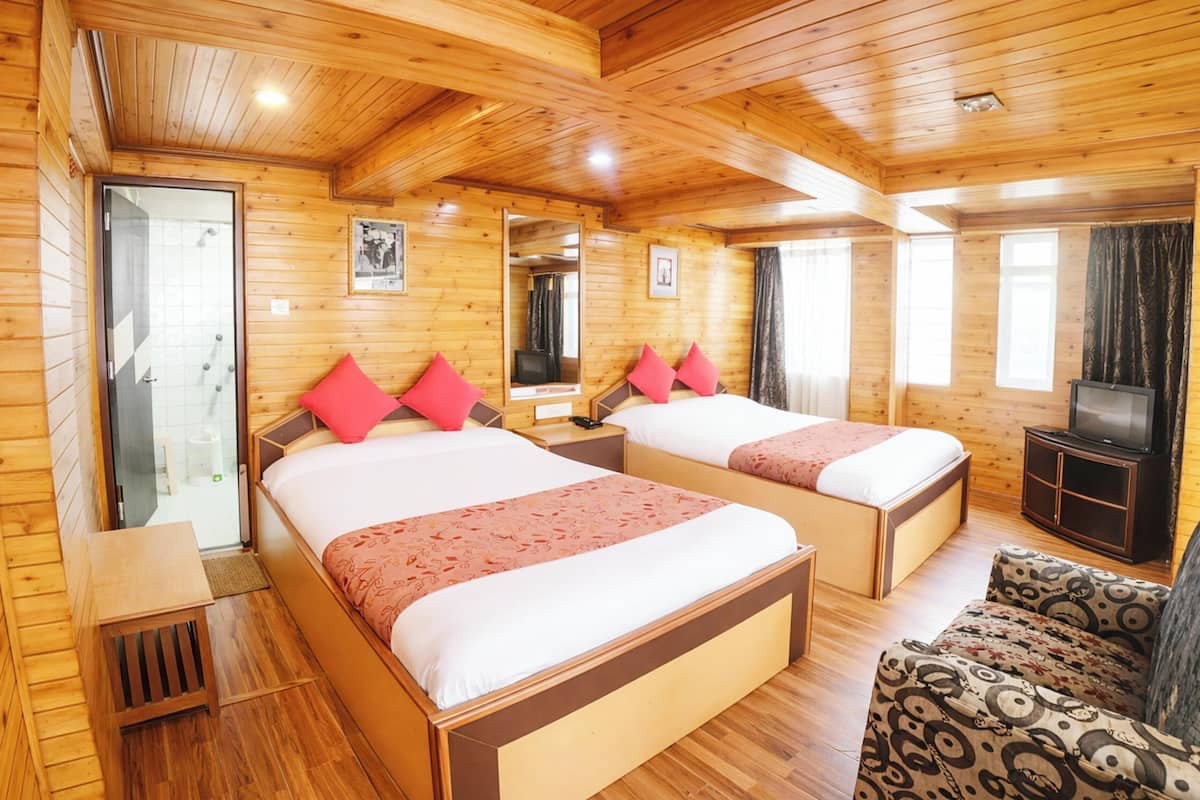 A wooden cabin room with two beds, a sofa, a TV, and a shower area.