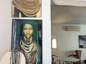 Ein Zimmer mit einem Gemälde einer Person in traditioneller Kleidung, einem Esstisch mit Stühlen und einer Wand-Klimaanlage.
