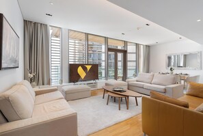 A modern living room with a sofa, ottoman, coffee table, and a flat-screen TV. - Vogue | Bluewaters Residences steps away from Ain Dubai and Wharf Mall (Dubai)