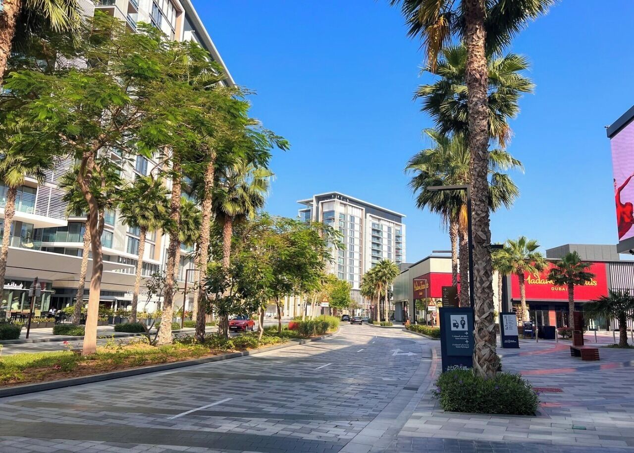A modern urban street with palm trees, a clear blue sky, and a building with a red sign.