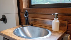 A bathroom with a wooden countertop, a stainless steel sink, a soap dispenser, and a window above the sink. - Luxury Covered Wagon Stay • Firepit, Views, Stargazing (Sevierville)