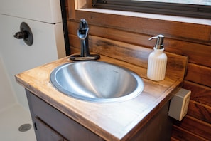A bathroom with a stainless steel sink, wooden countertop, and a window above the sink. - Lux Glamping Wagon - with A/C, WIFI, Full Bath (Sevierville)