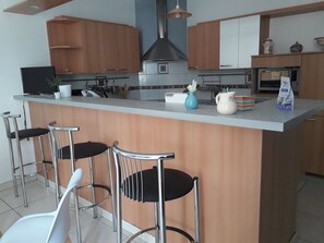 Eine moderne Küche mit einer zentralen Kochinsel, Barhocker und verschiedenen Küchengeräten.