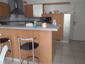 A kitchen with a central island, bar stools, and a refrigerator. - Roommate (Les Garennes sur Loire)
