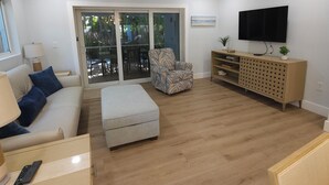 A living room with a sofa, ottoman, armchair, wooden cabinet, TV, and a ceiling fan. - Welcome to Hidden Oasis, your dog-friendly home away from home in Sanibel! (Sanibel)