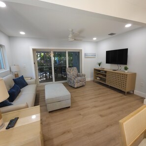 Ein Wohnzimmer mit Sofa, Hocker, Sessel, Holzschrank, Fernseher und Deckenventilator.