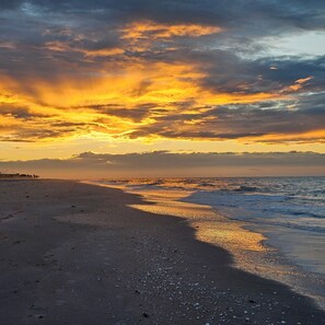 Ein Strand mit Sonnenuntergang, Wellen und wolkenlosem Himmel.