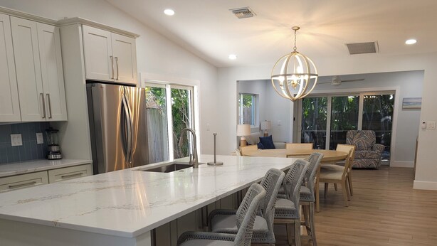 A modern kitchen with a large island, wooden chairs, and a chandelier. - Welcome to Hidden Oasis, your dog-friendly home away from home in Sanibel! (Sanibel)