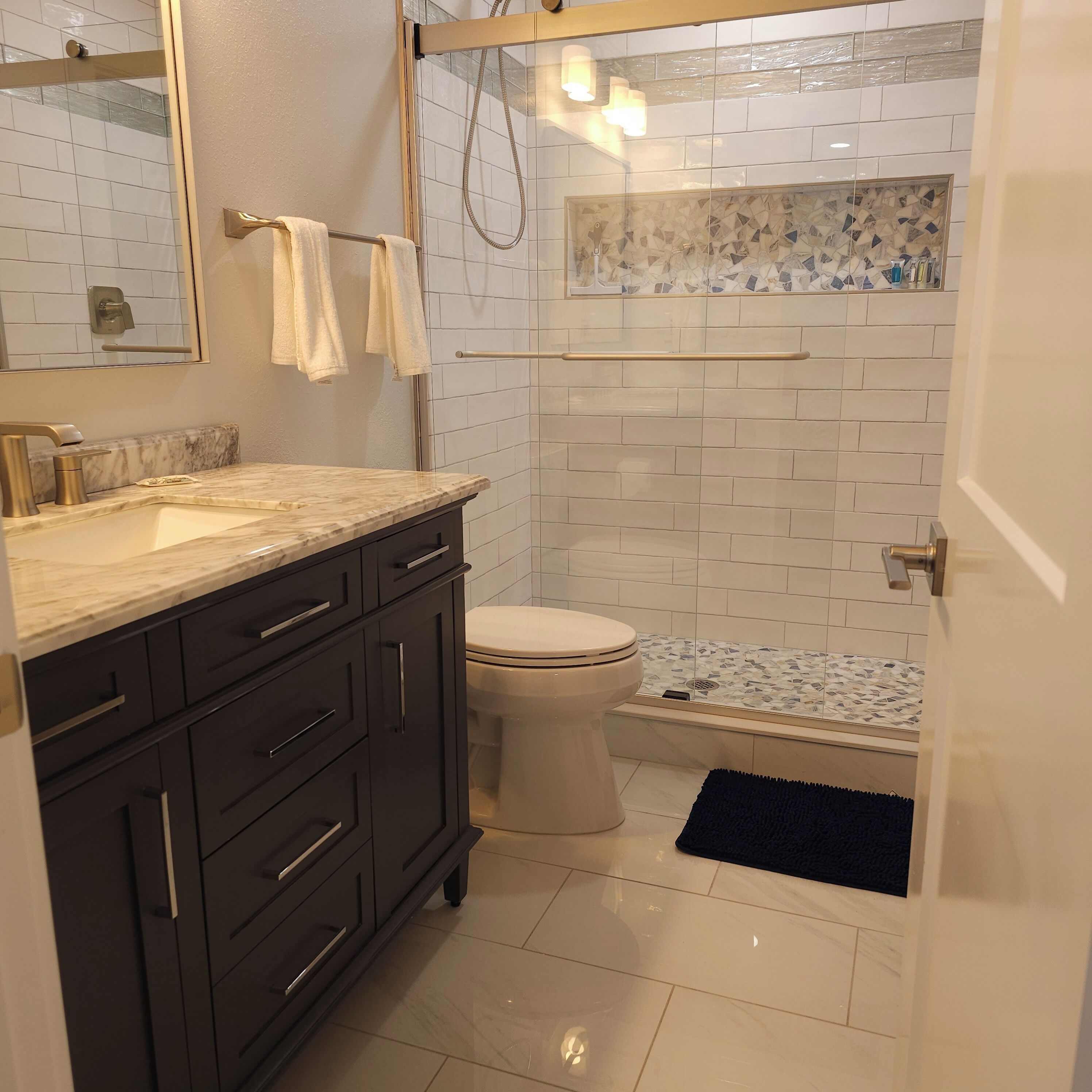 A modern bathroom with a marble countertop, a toilet, a glass-enclosed shower, and a tiled floor.