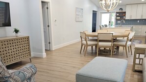 A modern living room with a dining area, wooden flooring, and a large grey ottoman. - Welcome to Hidden Oasis, your dog-friendly home away from home in Sanibel! (Sanibel)