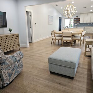 Ein modernes Wohnzimmer mit Essbereich, Holzboden und einem großen grauen Pouf.