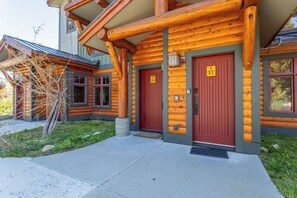 A log cabin with two red doors, a concrete walkway, and a small porch area. - Beautiful 2/2 Golf/Ski Condo-Garage, Jacuzzi, BBQ! (Mammoth Lakes)