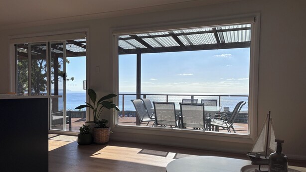 Una habitación con un ventanal grande que da a una terraza con asientos exteriores y vistas al mar.