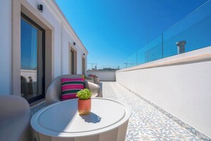 Une terrasse sur le toit avec une table ronde, des chaises, un pot de fleurs et un coussin coloré.