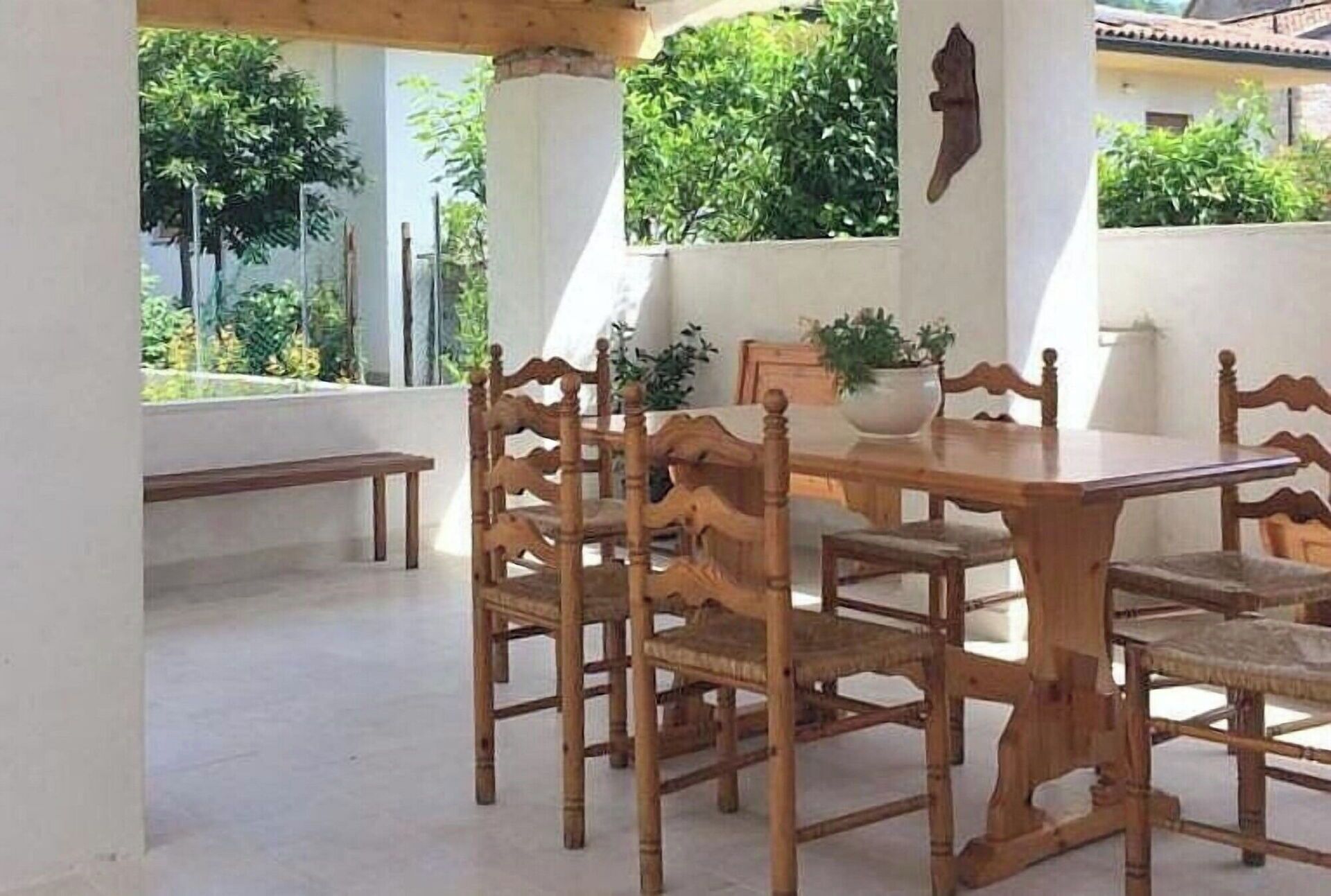A wooden dining table with chairs, a bench, and a potted plant on a balcony with a view of greenery.