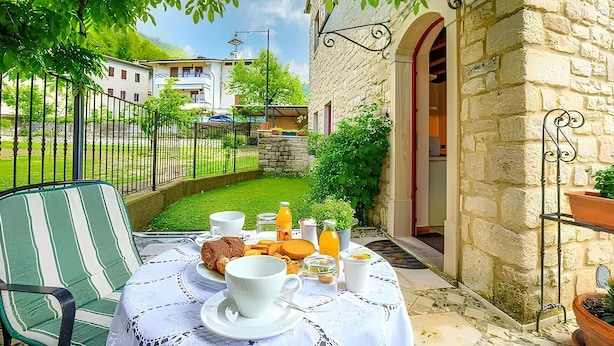 Eine Terrasse mit Frühstückstisch, gedeckt mit Gebäck, Kaffee und Saft, umgeben von Steinmauern und Grünpflanzen.