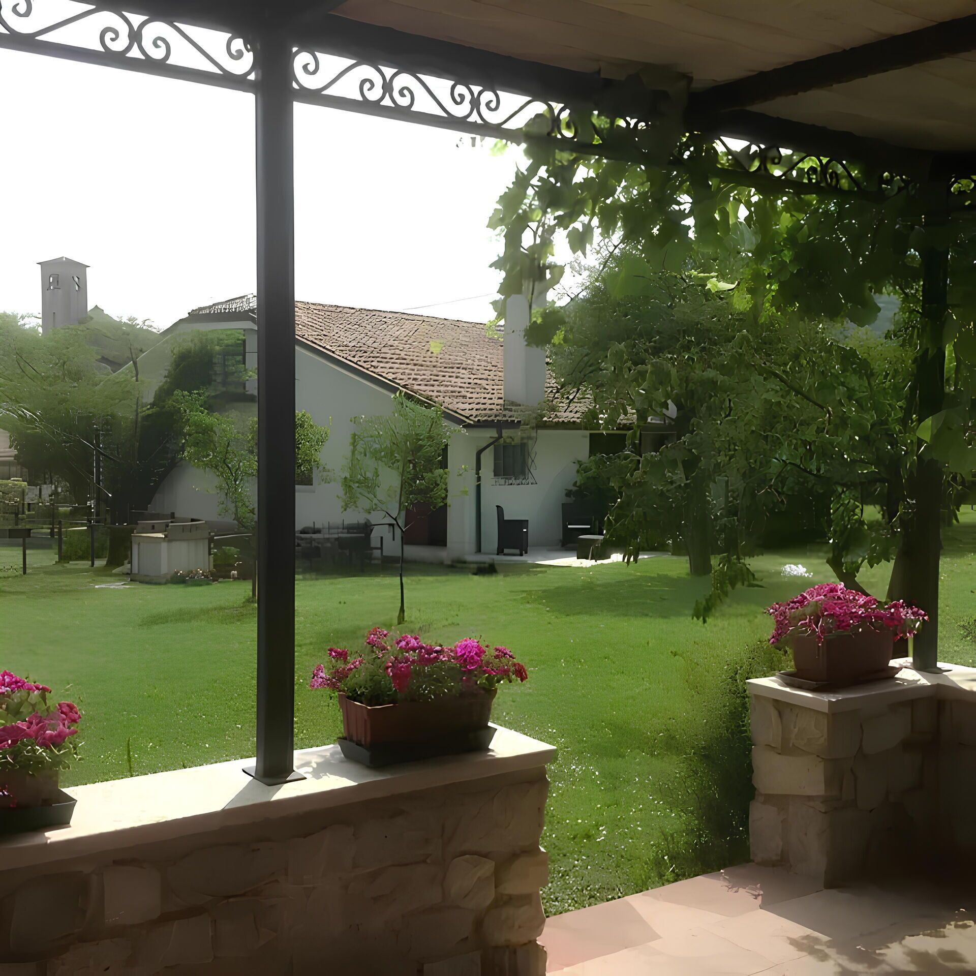 Een overdekt terras met stenen muren, potplanten en uitzicht op een huis met een pannendak.