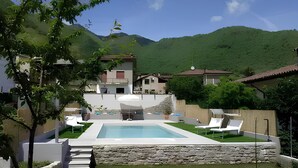 Ein Pool mit Liegestühlen, eine Steinmauer und Häuser in einer gebirgigen Gegend.