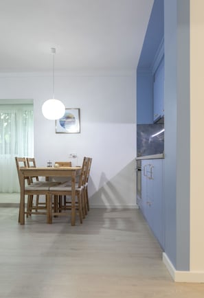 Et spiseområde med et træbord og stole, en hængende lampe samt et køkken med blå skabe.
