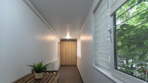 A narrow hallway with a wooden bench and a potted plant, leading to a door with a window on one side.