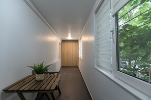 A narrow hallway with a wooden bench and a potted plant, leading to a door with a window on one side. - Imedio Azure Apartment Aviatiei (București)