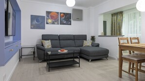 A modern living room with a grey sofa, a small table with a plate, and a dining area with a wooden table and chairs.
