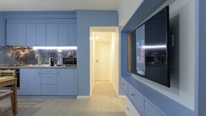 A modern kitchen with blue cabinets, a marble backsplash, and a flat-screen TV mounted on the wall.