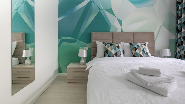 A hotel room with a geometric wall design, a bed with white linens, two bedside tables with lamps, and a mirror.