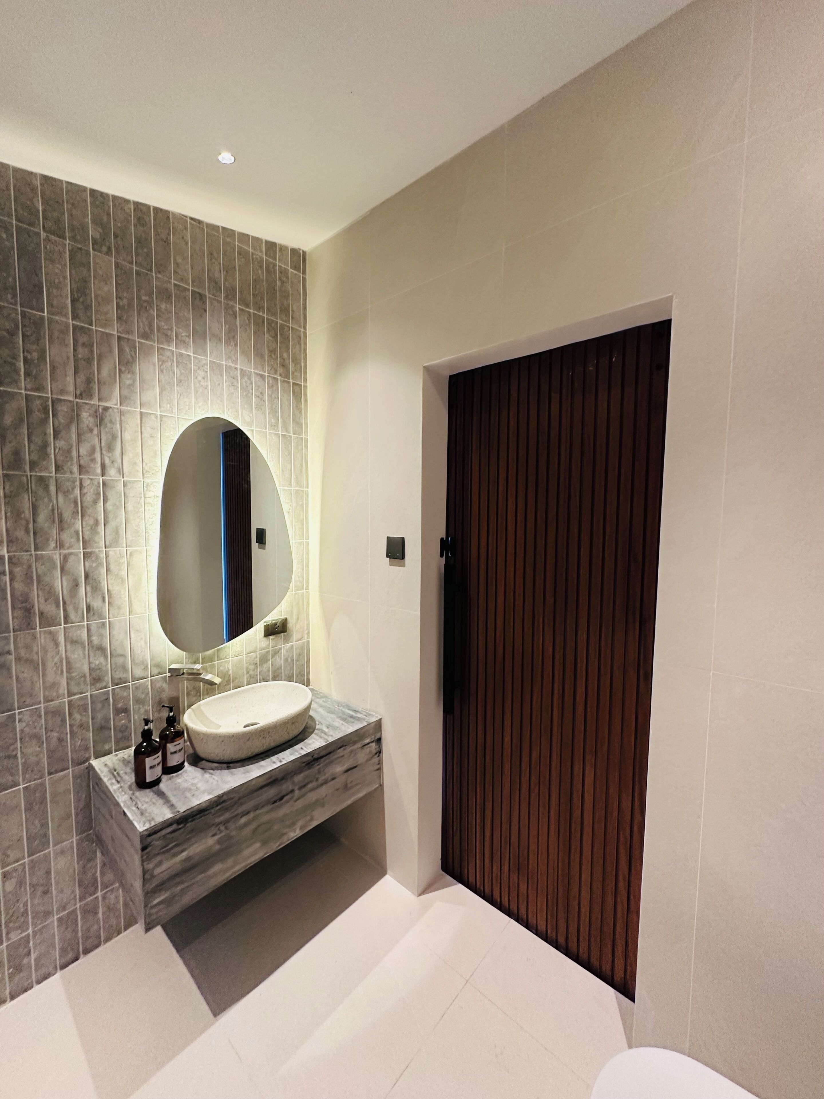 Un baño moderno con un espejo grande, un lavabo redondo y una puerta de madera.