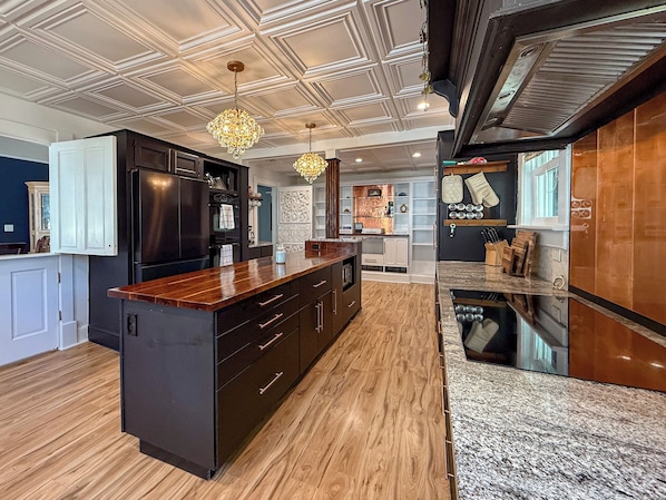 A modern kitchen with a central island, dark cabinetry, and a wooden countertop.