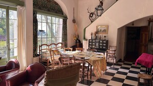 Une salle à manger avec un sol à carreaux, des chaises en bois, une table dressée pour quatre personnes et une fenêtre avec des rideaux.