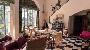 A dining room with a checkered floor, wooden chairs, a table set for four, and a window with curtains. - Beautiful Provencal house, 6 bedrooms, Tennis - At the foot of Mont Ventoux (Saint-Hippolyte-le-Graveyron)