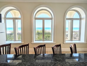 Ein Essbereich mit einem Marmortisch und Holzstühlen, drei Bogenfenster mit Blick auf den Strand.