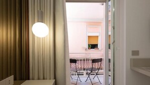 Una stanza con un letto, un comodino, una lampada a sospensione e vista su un balcone esterno con sedie.